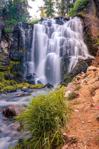 Kings Creek Falls Vertical composition of Kings Creek Falls in Lassen Volcanic National Park, photographed on a late summer afternoon. The image captures the 40-foot cascade spilling gracefully over dark volcanic rock, with silky white water contrasting beautifully against the lush green foliage and forest backdrop. Created using a long exposure technique, the flowing water takes on a smooth, ethereal texture that enhances the sense of tranquility and motion. This fine art nature photograph celebrates one of Lassen’s most scenic spots—an area forever changed by the 2021 Dixie Fire but remembered here in its pristine beauty. Ideal for nature lovers, hikers, and collectors of Northern California landscape photography.