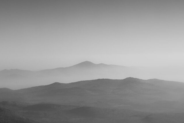 Dreamy and surreal, this black and white landscape photograph titled “Dreamy Vista” was captured from the summit of Fredonyer Peak in Lassen County, California, on September 1, 2021, while the massive Dixie Fire burned miles away. Viewed from nearly 7,950 feet, the scene reveals soft, undulating mountain ridges fading into layers of distant haze, created by smoke trapped in a morning atmospheric inversion. The muted tones and gentle gradients evoke a sense of calm despite the destruction beyond the horizon. This fine art image transforms a moment of environmental devastation into a study in light, depth, and quiet beauty — a minimalist vision shaped by nature’s raw forces.