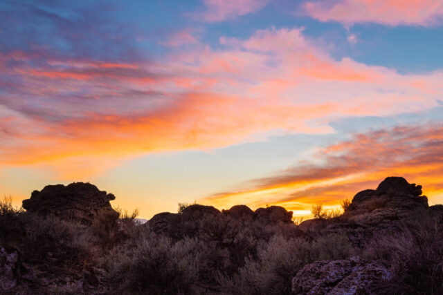 Vivid sunset landscape photograph of tufa formations near Wendel in Lassen County, California, showcasing the striking geology of the Honey Lake Valley. The sky ignites with brilliant hues of orange, pink, and violet as the sun sets behind the rugged limestone deposits—ancient remnants of underwater springs from the long-vanished Lake Lahontan. Silhouetted against the glowing horizon, the tufa mounds and desert vegetation add rich texture and depth to the scene. This fine art image captures the timeless beauty and geological history of Northern California’s high desert, where light, color, and ancient stone converge in a moment of serene grandeur.