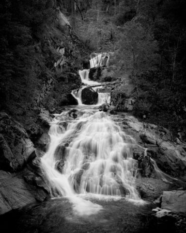 Whiskeytown Falls in Black and White Black and white photograph of Whiskeytown Falls on Crystal Creek in Shasta County, California. Captured on a quiet November morning, the 220-foot cascade flows gracefully down rugged rock terraces in soft, silky ribbons, enhanced by long exposure. The shaded canyon and overcast light lend the scene a naturally moody atmosphere, emphasizing texture, contrast, and the waterfall’s elegant movement. A timeless monochrome landscape that embodies serenity and strength, perfect for collectors of fine art nature photography or anyone drawn to the quiet grandeur of Northern California’s hidden waterfalls.
