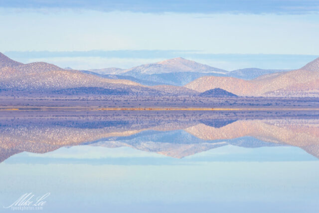 Peaceful winter landscape photograph of Mono Lake in California, showcasing the mirror-like reflections of softly lit mountain ridges across completely still water. Captured on a calm January evening, the telephoto composition emphasizes balance and symmetry, with pastel hues of lavender, rose, and blue forming layered patterns across the scene. The tranquil surface creates a perfect visual echo of the surrounding terrain, highlighting Mono Lake’s surreal beauty and natural harmony. This fine art image celebrates minimalism, serenity, and the quiet perfection of light and reflection in the Eastern Sierra.