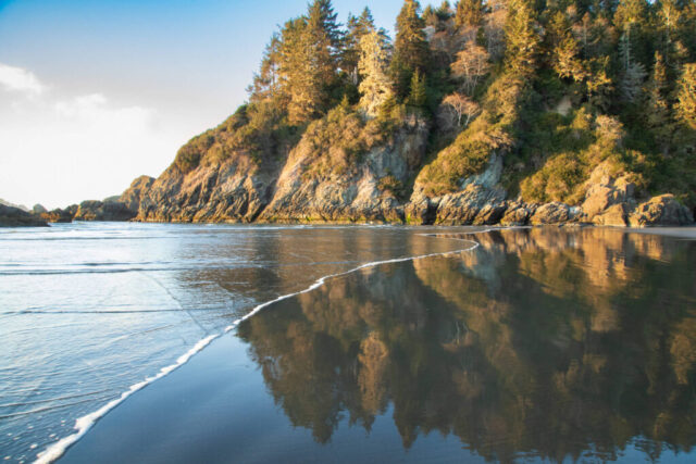 Soft light glows across Moonstone Beach near Trinidad in Humboldt County, California, where wet sand mirrors the warm hues of a February sunset. Gentle waves sweep far up the beach’s shallow gradient, leaving reflective patterns that shimmer beneath the cliffs at the north end. This serene coastal scene captures the tranquil beauty of California’s North Coast, where sea stacks rise offshore and the Little River meets the Pacific. A favorite destination for photographers, surfers, and nature lovers, Moonstone Beach offers a perfect blend of rugged geology, tidal reflections, and peaceful seaside atmosphere—ideal for coastal wall art and anyone who cherishes Humboldt County’s wild shoreline.