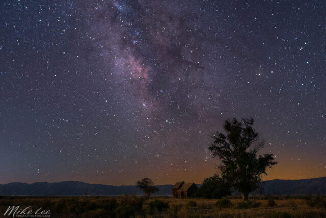 The Old Barn Under the Stars Astrophotography image of the Milky Way rising over an old barn in Lassen County, California. Captured on a warm August evening during a brief window of full astronomical darkness before moonrise, this wide-angle composition showcases the vibrant galactic core glowing in shades of violet, magenta, and blue against a field of countless stars. The barn, a familiar local landmark nestled in the Honey Lake Valley, sits small but grounded beneath the vast night sky, illuminated softly by the rising 85% moon. Multiple frames of the sky were stacked to reduce digital noise and blended with a single long exposure of the foreground, creating a seamless balance between celestial brilliance and rustic quiet. The result is a tranquil portrait of rural Northern California under the Milky Way, complete with the haunting soundtrack of distant coyotes.