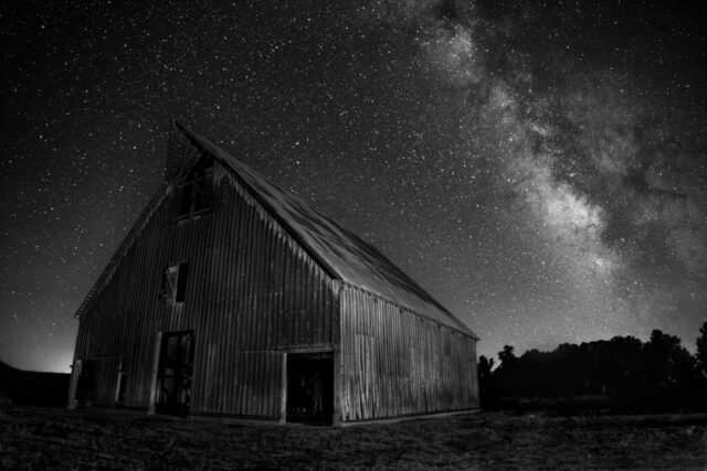 Olson Barn Nightscape Black and white version – Monochrome nightscape of the Olson Barn near Chester, California, silhouetted beneath the glowing band of the Milky Way. The barn’s aged timber siding and angular roof stand in stark contrast to the luminous river of stars streaming across the night sky. Without color, the image emphasizes form, texture, and light—the interplay between the barn’s historic structure and the timeless expanse of the cosmos. A fine art interpretation that distills the quiet essence of this iconic Feather River Land Trust landmark and the vast Sierra night above Lake Almanor.