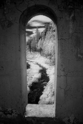 Window to the Susan River Black and white infrared photograph taken through an arched opening of the abandoned 1923 Devil’s Corral Bridge overlooking the Susan River Canyon in Lassen County, California. Captured with a full-spectrum camera and an 830nm deep infrared filter, the image transforms the rugged landscape into a surreal monochrome scene, where bright, ghostly foliage contrasts sharply with the dark stone textures of the bridge’s weathered Art Deco architecture. The composition uses the archway as a natural frame, creating a striking “window” view of the canyon and sky beyond — a hauntingly beautiful blend of history, decay, and timeless wilderness.