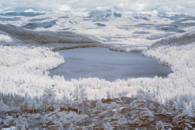 Infrared landscape photograph of Donner Lake and the Sierra Nevada mountains near Truckee, California, captured with a 720nm near-infrared filter on a full spectrum modified camera. The snow-dusted forest and peaks appear bright white while the deep blue lake contrasts below, creating a surreal, high-elevation vista in invisible light.