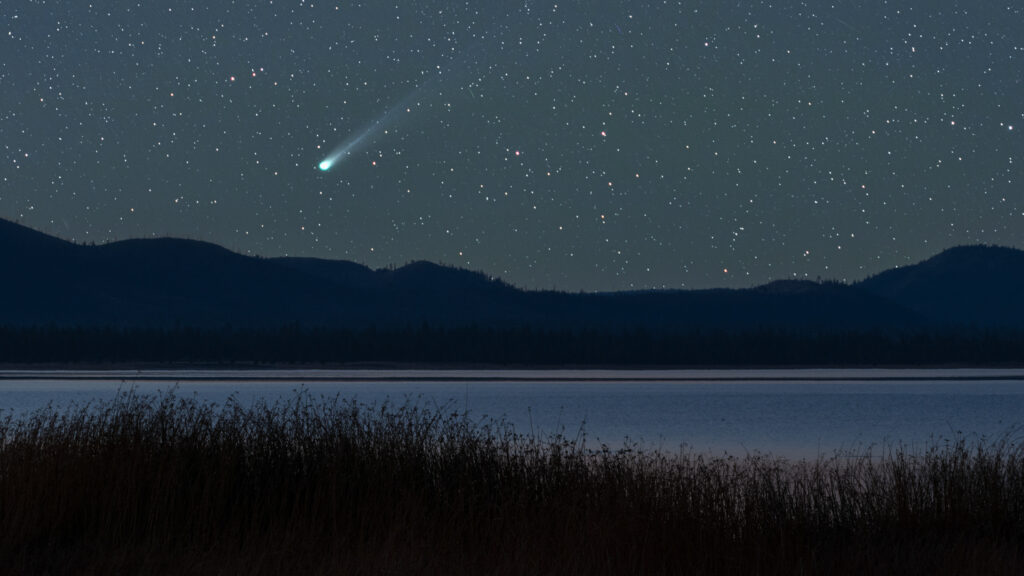 Night sky photograph of Comet C/2025 A6 (Lemmon) captured over Eagle Lake in Northern California on October 18, 2025. The comet’s bright green nucleus and long, tapering dust tail glow vividly against a star-filled sky, rising above the silhouetted ridgeline and still waters of the lake. Foreground grasses and the calm reflection of twilight lend a sense of quiet isolation and vastness. Shot using a tracking mount for precise long exposure, this astrophotography image showcases the beauty of a rare celestial visitor and the pristine darkness of Eagle Lake’s remote landscape. A fine art nightscape blending cosmic wonder with the tranquil mood of the high desert wilderness.