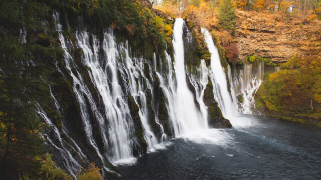 Autumn Morning at Burney Falls Fine art landscape photograph of Burney Falls in McArthur-Burney Falls Memorial State Park, Shasta County, Northern California, captured on a crisp autumn morning. The image showcases the iconic multi-tiered waterfall cascading over moss-covered basalt cliffs, framed by golden and amber foliage at the height of fall color. Soft dawn light enhances the contrast between the cool, silky flow of the water and the warm tones of the surrounding forest, creating a serene and balanced composition. Often called the “Eighth Wonder of the World,” Burney Falls is celebrated here in its tranquil seasonal glory — an ideal piece for lovers of waterfalls, autumn landscapes, and the natural beauty of Northern California.