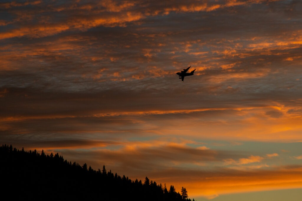 Silhouette of a C-17 aircraft flying above Eagle Lake near Miner’s Point in Lassen County, California, set against vivid orange and gray sunset clouds.