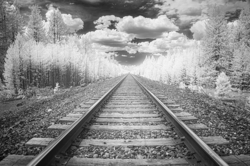 Infrared black-and-white view of Burlington Northern Santa Fe railroad tracks leading through forest in Lassen County, California.