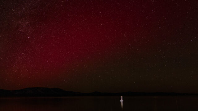 Magenta Aurora Over Eagle Lake Magenta aurora borealis reflected in Eagle Lake, California, with a lit navigational buoy in the foreground and star-filled sky above dark shoreline silhouettes.