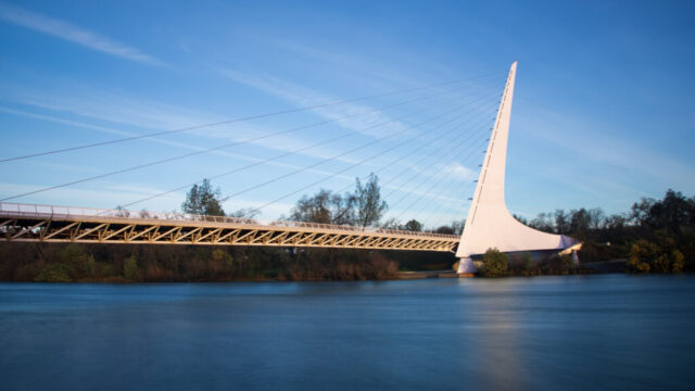 Sundial Bridge Morning – Redding - Shasta County California Sundial Bridge spanning the Sacramento River at dawn in Redding, California, with its white cable-stay pylon reflected in long-exposure water below a clear winter sky.