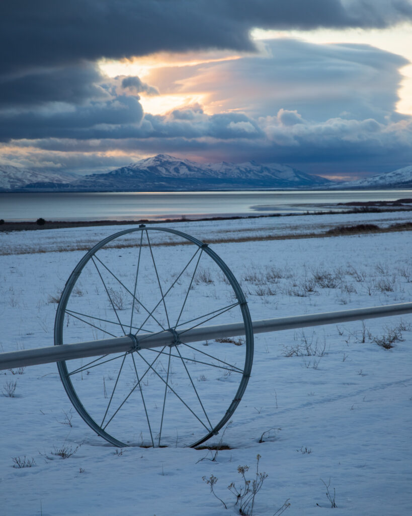 Single irrigation wheel line in snow-covered Honey Lake Valley hay field with lenticular cloud and storm sky, Lassen County, California
