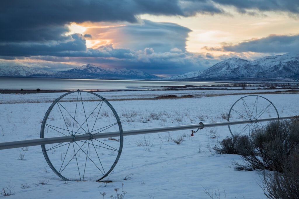 Irrigation wheel line in snowy Honey Lake Valley hay field with lenticular cloud over Sierra Nevada, Lassen County, California